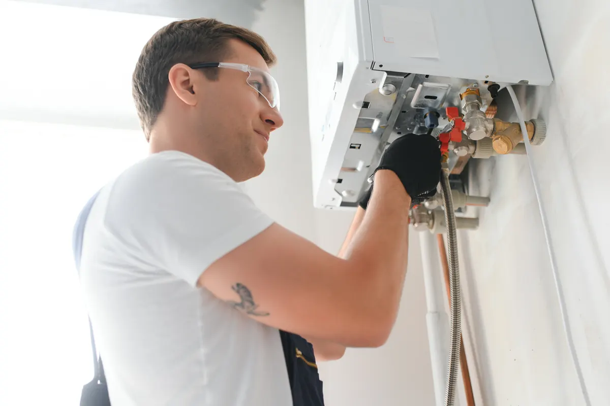 Heating technician checking a gas valve on a wall-mounted boiler during an emergency no-heat call